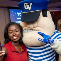 Girl in a red dress takes a selfie with Louie the Laker mascot.